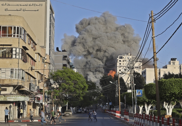 People run away from the vicinity of Al-Sharouk tower as it collapses after being hit by an Israeli air strike, in Gaza City, on May 12, 2021. © Mohammed Abed / AFP